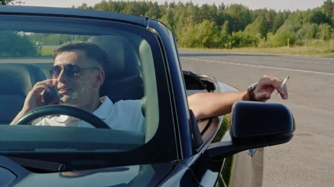 Man talking on smartphone while smoking cigarette in convertible car 库存影片 266492520