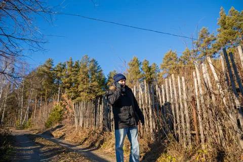 Man talking on smartphone while walking on path in village. Male in winter Stock Photos