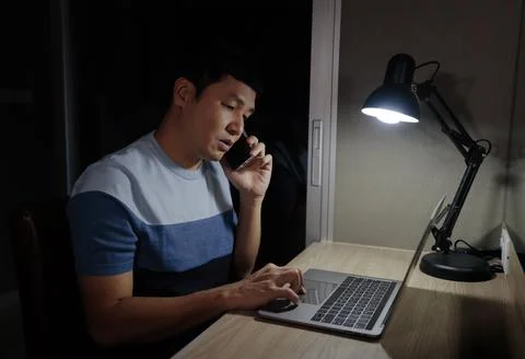 Man talking with smartphone while working with laptop at night Stock Photos