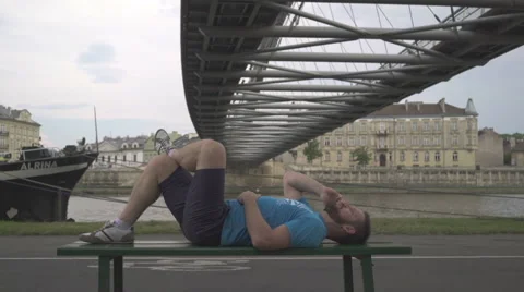 Man is talking by smatphone, lying on the bench against the river. Vidéo 65187887