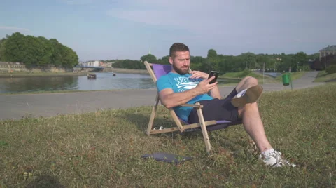 Man is talking by smatphone, lying on sunbed by the river. Vídeos de archivo 65205443