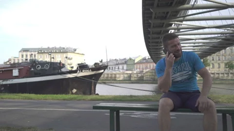 Man is talking by smatphone, sitting on the bench, pan shot. Vídeo Stock 65205124