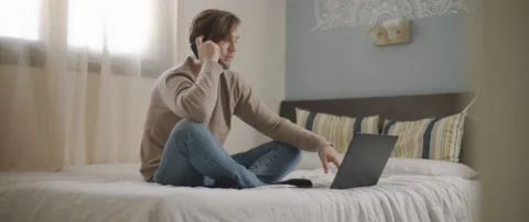 A man talking to someone on the phone while working with a laptop from home. Stock Footage 135096028