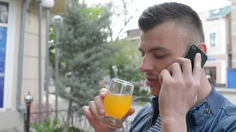 Man talks to a Mobile Sell Phone, drinking Orange Juice, street town Video stock 62294584