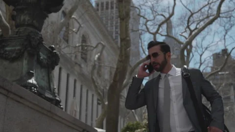 Man talks on phone while walking through city streets during daytime Stock Footage 312685760