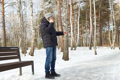A man talks on the phone while walking in a snowy winter park Stock Photos