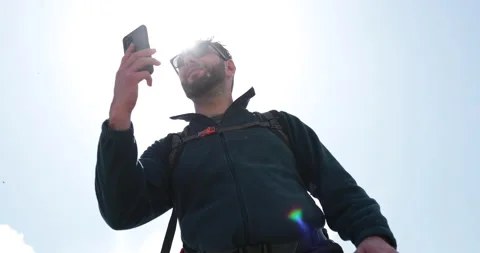 A man talks to someone on the phone while standing with a backpack while hiking. Stock Footage 250789366