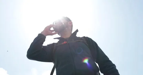 A man talks to someone on the phone while standing with a backpack while hiking. Stock Footage 250789615