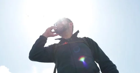 A man talks to someone on the phone while standing with a backpack while hiking. Stock Footage 250790318