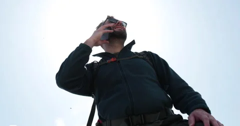 A man talks to someone on the phone while standing with a backpack while hiking. 動画素材 250790515