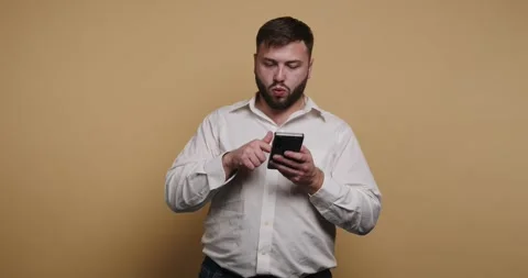 Man talks while holding phone and gestures with one hand in a simple studio.. Vídeo Stock 326797626