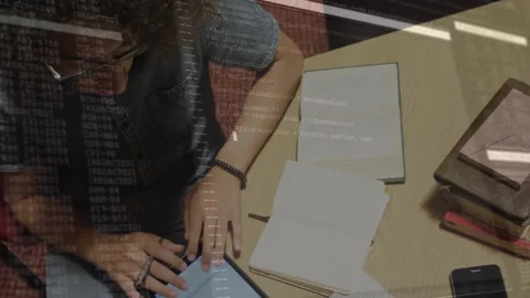 Man tapping blue tablet and referencing notebook while reviewing code overlay Stock Footage 311916376