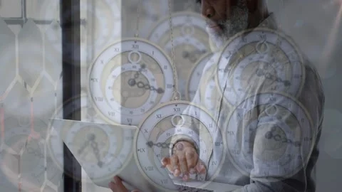 Man tapping laptop by window pausing reflecting as vintage clocks overlaying Stock Footage 328230227