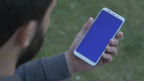 Man tapping on menu at bottom of blue screen phone, over the shoulder shot Stock Footage 105129381