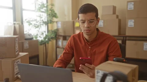 Man tapping smartphone and checking orders among stacked shipping boxes in .. Stock Footage 339199525