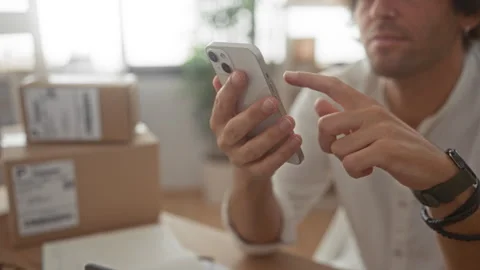 Man tapping smartphone with index finger among cardboard shipping boxes in .. Stock Footage 339220258