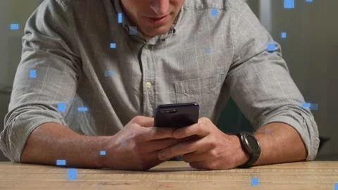 Man tapping smartphone at table, browsing tech content while blue squares Stock Footage 333609788