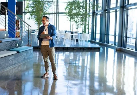 Man tapping tablet in office lobby, spawning animated charts over polished floor Stock Photos