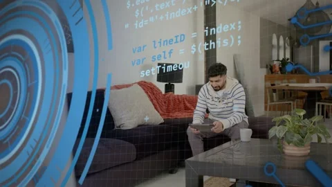 Man tapping tablet on sofa, bringing up blue HUD and scrolling code overlays for Stock Footage 334202515