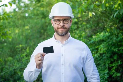 Man taskmaster in hardhat showing blank contact card outdoors, copy space Stock Photos