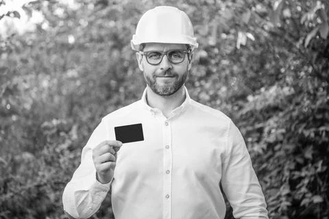 Man taskmaster in hardhat showing blank contact card outdoors, copy space Stock Photos