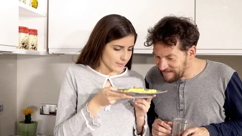 Man tasting omelette cooked by girlfriend in kitchen in pajamas Stock Footage 75281206