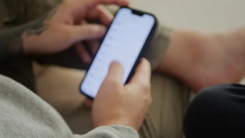 Man with tattooed hands using a smartphone, scrolling and tapping... Stockbeeldmateriaal 318177702