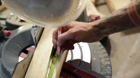 Man with tattoos measuring and marking a 2x4 piece of wood on a mitre saw 库存影片 40648078