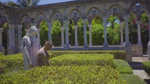 Man with tattoos stands in front of a statue among ancient columns with his head Stock Footage 112697875