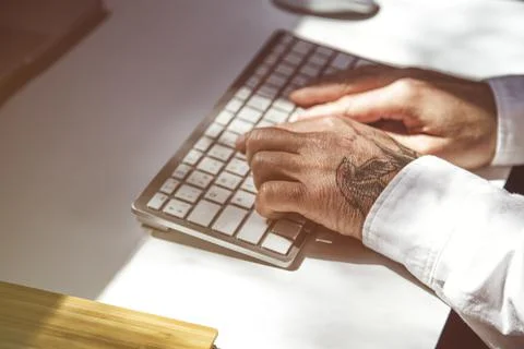 Man with tattoos using laptop at office table Stock Photos
