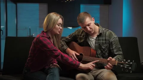 Man teaching woman how to playing guitar in home interior.Couple doing education Stock Footage 225657451