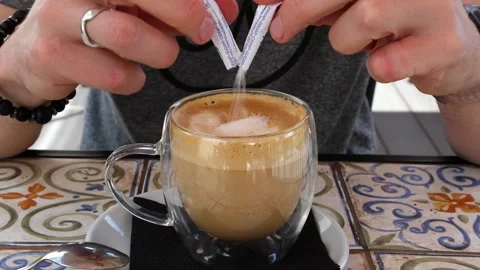 A man tears a stick of sugar and pours it into a cup of coffee. 스톡 동영상 245360034