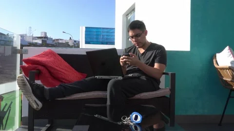 A man telecommuting from a beach house with his laptop and cell phone in the Stock Footage 155825481