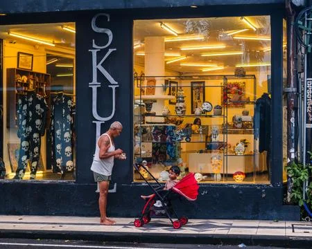 Man Tending to Child in Red Stroller Outside Skull Boutique Foto stock
