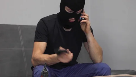 Man terrorist in mask talking on the phone with gun in hand and grenade on the t Stock Footage 97765900