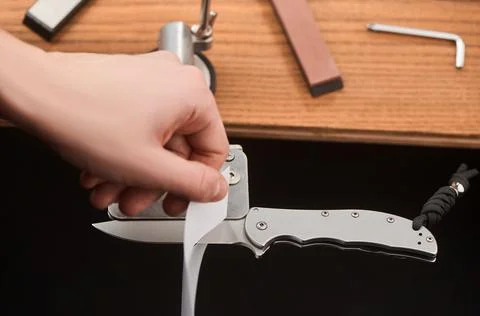Man testing the blade of a folding knife with a paper sheet Stock Photos