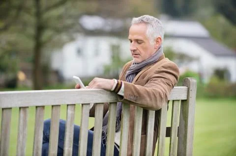 Man text messaging on a mobile phone in a park Stock Photos