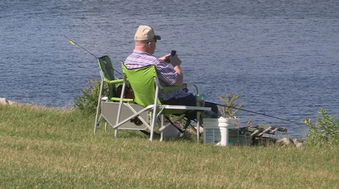 Man texting on a cell phone sitting by the lake fishin in cottage country Stock Footage 40028897