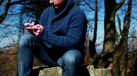 Man texting on the cellphone and sitting on the rock in the mountainous area 스톡 동영상 38481669
