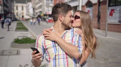 Man texting ona a phone while woman surprises waiting man by covering his eyes. Stock Footage 41479987
