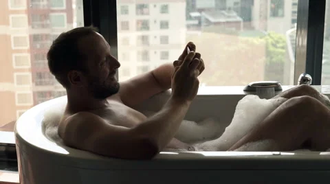 Man texting sms on smartphone sitting in the bathtub Видео 60735777