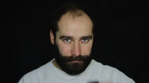A man with a thick beard shaves, removes hair on his head with an electric razor Stock Footage 143808832