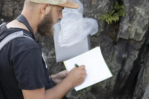 Man thinks and writes a visit in a geocaching workbook Stock Photos