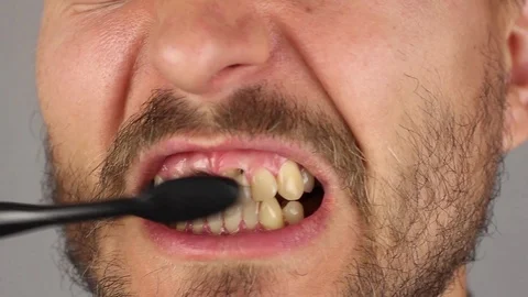 Man thoroughly brushes teeth with black toothbrush, movements from side to side Stockbeeldmateriaal 94927105