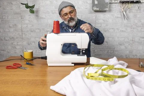 Man threading sewing machine creating clothes at home Stock Photos