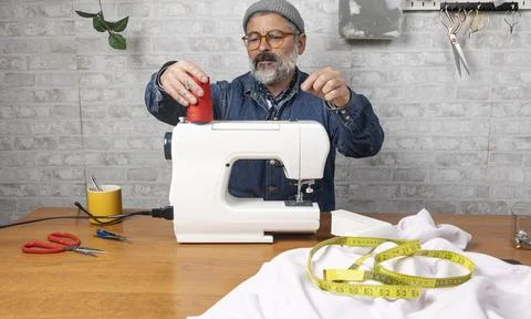 Man threading a sewing machine for tailoring project 스톡 사진