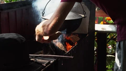 Man throw firewood into mangal. Pot of soup is hanging over the fire. Stock Footage 169150331