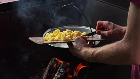 Man throw potatoes into soup in pot. Bonfire in mangal close-up Stock Footage 169150930