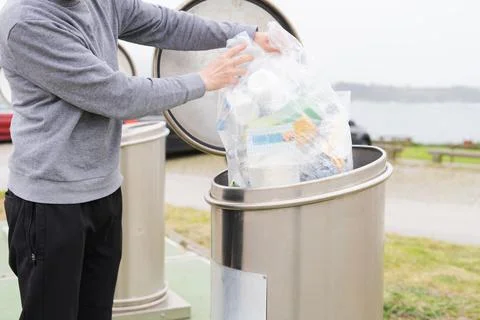Man throwing bag with plastic containers at recycling point. Stock Photos
