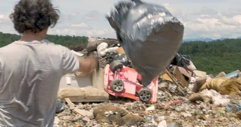 Man throwing a bag of trash and a broken office chair into the landfill Stock Footage 89344229